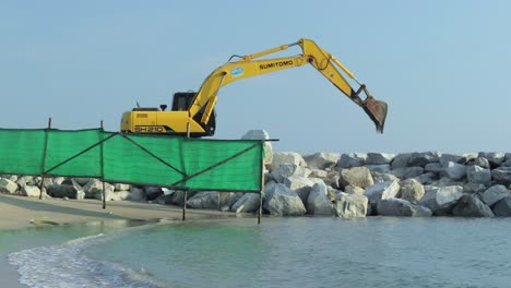Heavy-digging-machinery,-excavator-building-a-rock-wall-to-protect-the-harbour-from-storms-large-waves-or-a-tsunami