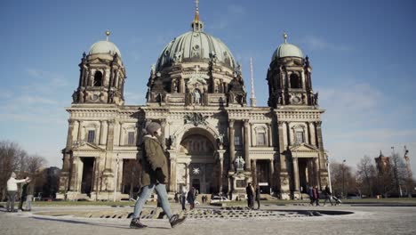 Girl-walking-past-Berlin-Cathedral-with-tourists-standing-outside,-slow-motion