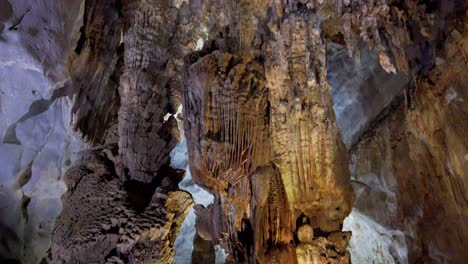 Massive-stalagmite-formation-lifts-from-the-cave-floor-as-a-visitor-walks-right,-Tilt-up-reveal-shot