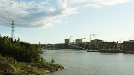 Aerial,-low,-drone-shot-towards-a-boat-driving-under-the-Isoisansilta-bridge,-between-Mustikkamaa-island-and-the-Kalasatama-district,-on-a-sunny-evening,-in-Helsinki,-Uusimaa,-Finland