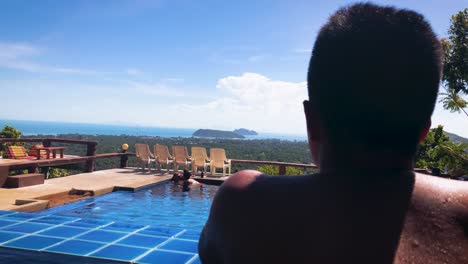 Man-Looking-At-The-Lovely-Couple-Bonding-In-The-Infinity-Pool-At-The-Secret-Garden-Cafe-In-Koh-Phangan,-Thailand---back-view