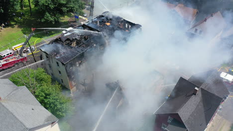 Ein-Wohnhaus-Schwelt-Nach-Einem-Brand-Mit-Feuerwehrleuten-Vor-Ort,-Rotierende-Luftaufnahme