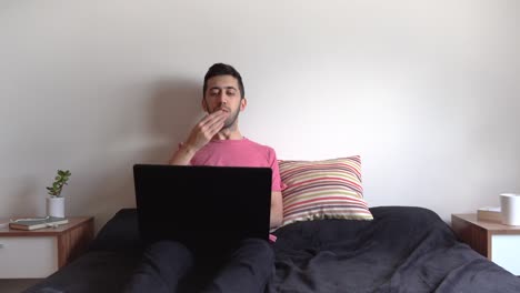 Man-laying-on-bed,-waving-at-the-screen-of-his-laptop-and-blowing-kisses