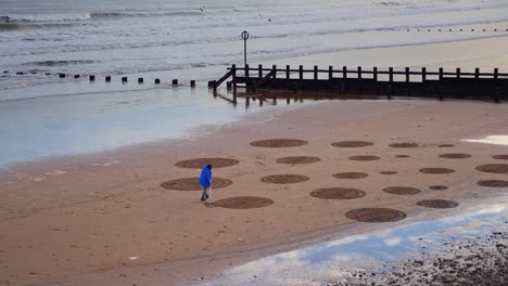 Man-creating-art-by-raking-sand-on-Aberdeen-beach-in-winter