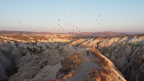 Wandern-In-Kappadokien-Bei-Sonnenaufgang-Mit-Bunten-Luftballons-Am-Himmel