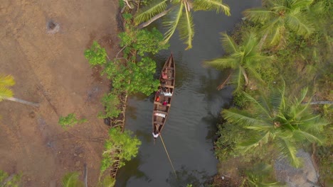 Aerial-view-of-long-boat-with-tourists-and-guides-canoeing-through-the-narrow-canals-and-waterways-of-Munroe-island,-India