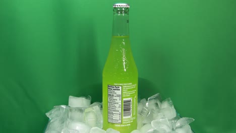 2-3-Botellas-De-Bebida-De-Lima-Jarritos-Que-Giran-360-Grados-Sobre-Hielo-Apilado-Frente-A-Una-Pantalla-Verde