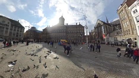 The-Royal-Palace-With-Pigeons-And-People-At-Dam-Square-In-Amsterdam,-Netherlands-On-A-Sunny-Morning---fisheye-view,-panning-shot