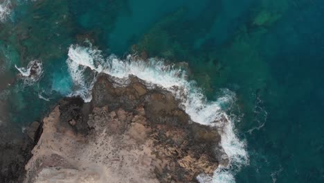 White-waves-crash-on-the-limestone-shore-contrasting-the-turquoise-waters-from-a-top-down-perspective