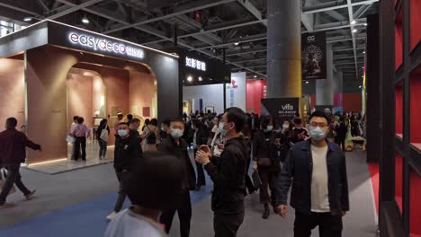People-wearing-masks-and-walking,-looking-around-in-between-product-pavilions-at-kitchen-design-exhibition-in-China,-during-COVID-19-Pandemic