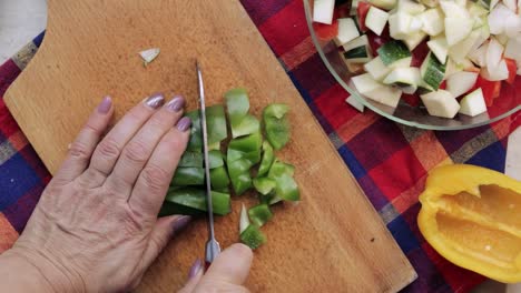 Top-down-view-of-woman's-hands-using-a-santoku-knife-and-slicing-green-sweet-pepper-on-a-wooden-cutting-board