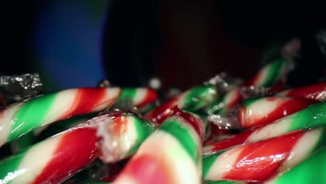 Moving-across-the-top-of-a-large-pile-of-wrapped-red,-white,-green-mini-candy-canes-while-the-background-cycles-different-colors