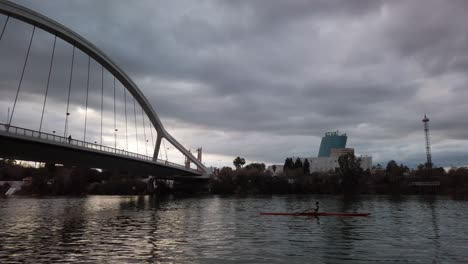 Silhouette-Person-Rows-River-Kayak-with-Stormy-Sky,-Panoramic-Pan-Right