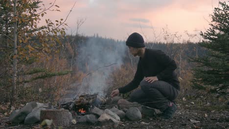 Woman-In-Black-Beanie-And-Sweatshirt-Making-Campfire-At-Alaska-Mountain-Campground-During-Sunset---Medium-Shot,-Slow-Motion