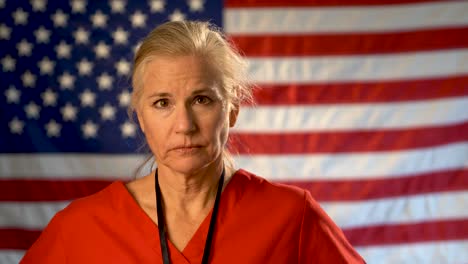 Female-nurse-walking-from-out-of-focus-US-flag-to-a-medium-tight-portrait-looking-very-sad,-worried-and-concerned