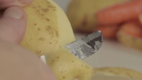Hände-Schälen-Kartoffeln-Mit-Karotten-Im-Hintergrund-Makroaufnahme