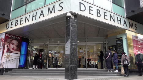 A-slow-motion-shot-of-shoppers-entering-and-leaving-Debenhams-department-store-as-people-stroll-along-Oxford-Street-on-the-first-morning-Covid-restrictions-on-the-second-national-lockdown-are-relaxed