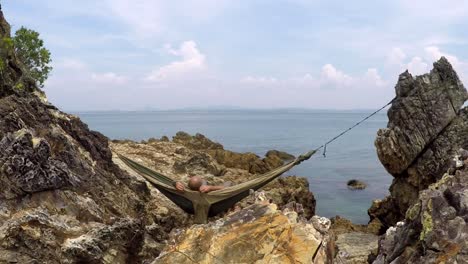 Man-relaxing-in-a-hammock-between-rocks-and-looking-at-the-sea