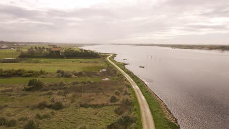 4K-aerial-view-of-a-dirty-road-in-the-bedside-of-Ria-de-Aveiro-in-the-estuary-of-river-Vouga,-drone-moving-forward,-boat-silhouette,-60fps