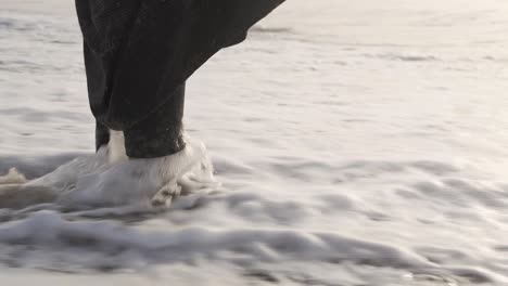 Close-up-of-foamy-sea-waves-splashing-female-feet-at-the-beach