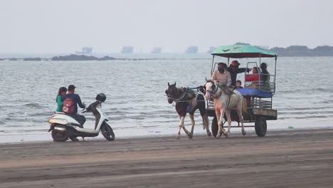 A-small-Asian-family-doing-horse-riding-in-horse-cart-on-beach-and-enjoying-holidays,-A-horse-cart-on-beach-during-sunset-with-a-small-group-of-people-in-it