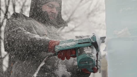 Ice-chips-and-shavings-spraying-out-of-ice-sculpture-as-artist-uses-electric-chainsaw,-Slow-Motion