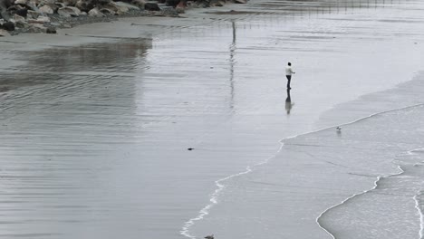Lone-person-strolling-up-the-beach-on-a-cold-day,-waves-rolling-ashore