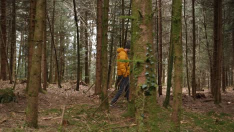 Young-european-man-with-bright-yellow-jacket-walks-in-forest,-sideways-dolly