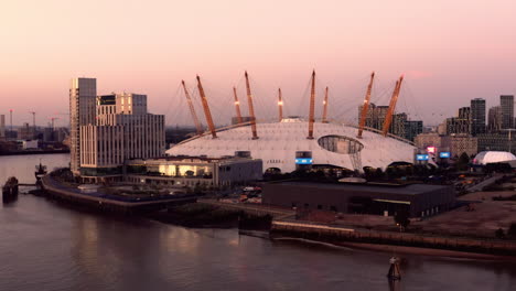 Aerial-view-of-the-O2-from-over-the-River-Thames-and-rotating-clockwise-around-the-peninsular,-showing-the-InterContinentalHotel-and-thelit-skies-shining-from-the-glass-of-the-building