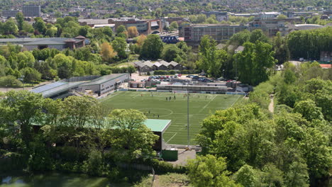 Aerial-establishing-shot-of-Maidstone-FC,-rise-over-trees-to-reveal-football-players-training-on-the-pitch