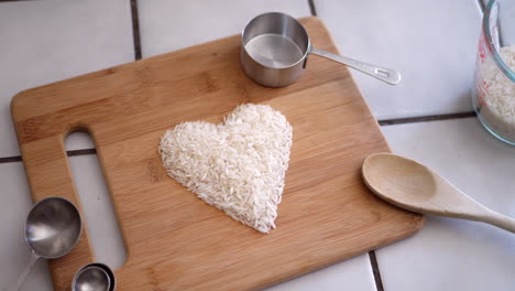 Grano-De-Arroz-Blanco-En-Un-Corazón-Con-Utensilios-De-Cocina-E-Ingredientes-En-Un-Tobogán-De-Cocina-A-La-Derecha