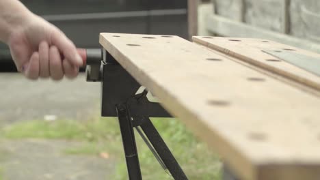Workman-hand-manually-turning-the-handle-of-a-wooden-workbench