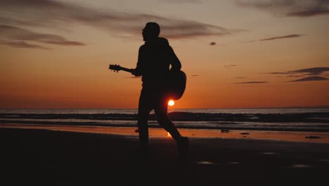 Mann-Läuft-Mit-Gitarre-Im-Hinteren-Sandstrand-Bei-Sonnenuntergang