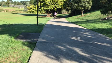 Cyclist-riding-at-a-quick-pace-down-a-concrete-pathway-in-a-park