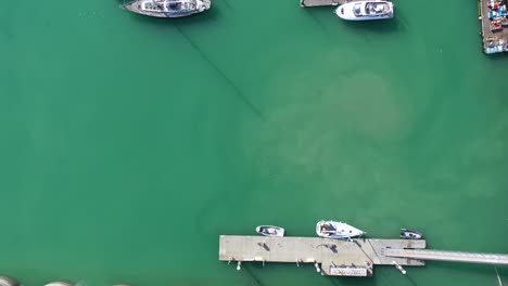 Top-down-aerial-view-of-sailing-boats-and-yachts-moored-on-the-turquoise-waters-of-Brighton-Marina,-UK-push-in-from-the-Harbour-wall