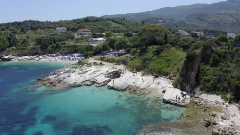 Aerial-drone-rising-view-revealing-Kassiopi-bays-people-swimming-and-sunbathing,-Corfu-Greece