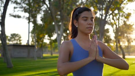 Eine-Schöne-Junge-Hispanische-Yogi-Frau,-Die-Bei-Sonnenaufgang-In-Einer-Einbeinigen-Gebetshände-Im-Park-Meditiert