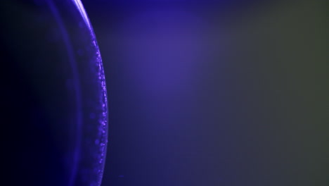 Macro-shot-of-small-particles-moving-counter-clockwise-on-a-purple-glowing-sphere