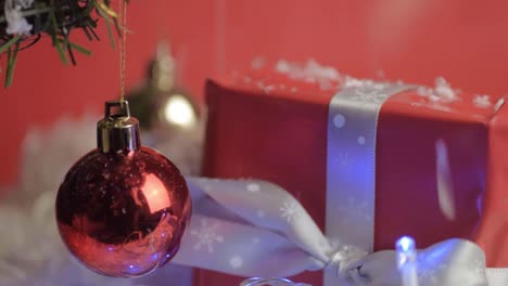 Christmas-baubles-and-gift-with-falling-fake-snow-and-fairy-lights-background