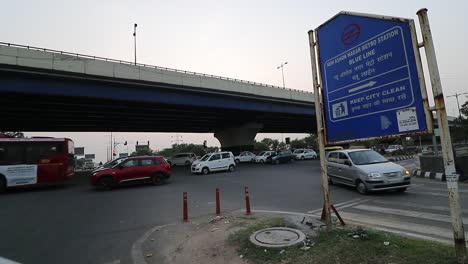 Traffic-passes-by-at-a-traffic-signal-under-a-flyover-in-New-Delhi,-India