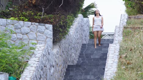 Young-brunette-woman-wearing-white-clothes-walking-down-the-stairs-in-tropical-area-on-windy-day