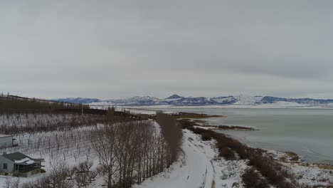 Flying-over-a-farm-near-the-shoreline-of-Utah-Lake-near-Lincoln-Beach,-looking-toward-the-west-mountains-as-seen-by-drone