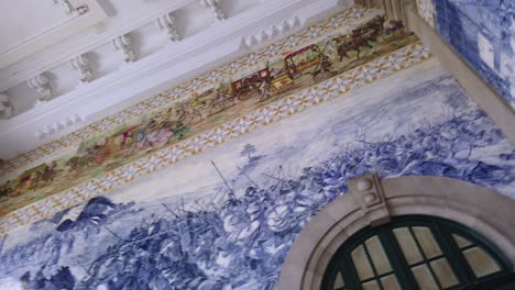Pan-left-to-view-upper-panels-of-azulejo-tile-art-in-Sao-Bento-Train-Station-in-Porto,-Portugal