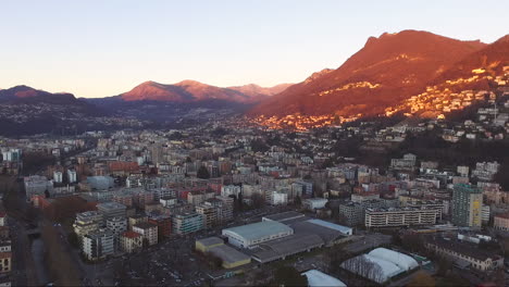 Aerial-view-of-a-beautiful-city-surrounded-by-mountains,-next-to-a-lake,-during-a-sunset-in-autumn