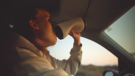 Young-blond-man-drinks-from-water-bottle-while-driving-in-the-light-of-the-setting-sun-in-the-car