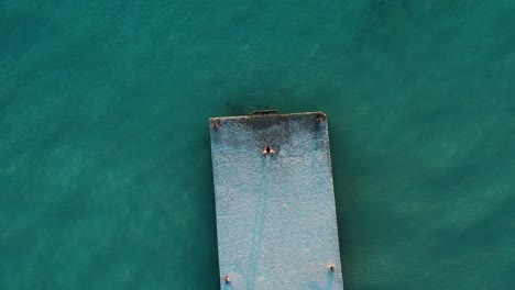 Drone-shot-directly-above-of-man-on-pier-looking-at-clear-blue-sea