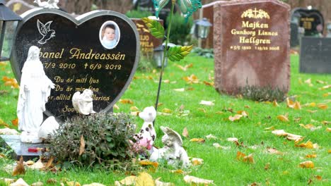 Young-boy's-tombstone-with-plants-and-Catholic-statues-in-Kviberg-Cemetery-in-Gothenburg,-Sweden