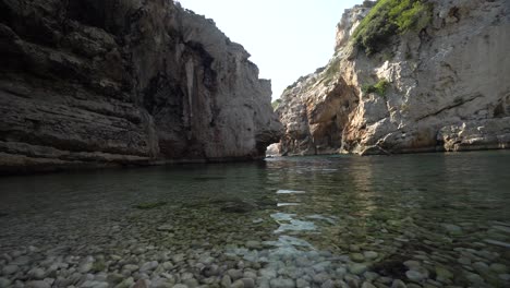 Low-angle-view-of-still-clear-water-of-the-sea-in-a-shaded-and-secluded-cove-hidden-by-tall-cliffs-along-the-coast-of-Croatia