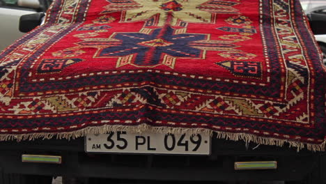 Front-view-of-parked-car-draped-with-colourful-handmade-rug-on-street-in-Yerevan,-Armenia