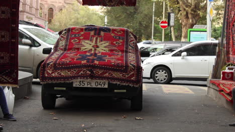 Front-view-of-parked-car-draped-with-colourful-handmade-rug-at-market-stall-in-Yerevan,-Armenia